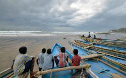 Children sit on fishing boats by the shore before being evacuated, at Visakhapatnam district