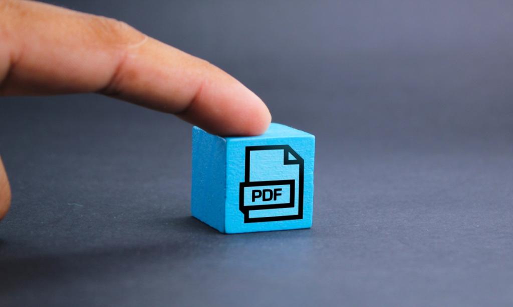 close up shot of a cube with the PDF logo and illustration drawn on it, pressed by a finger