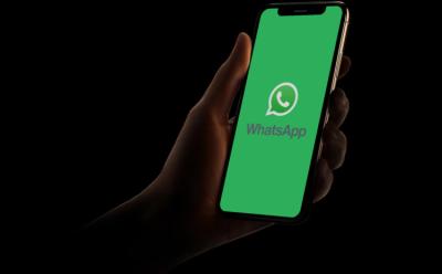 A hand holding an iPhone with the WhatsApp logo placed in a dark background