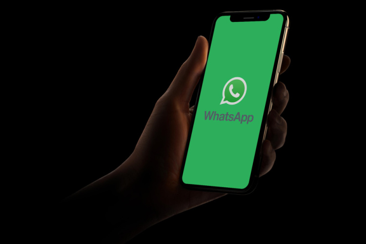A hand holding an iPhone with the WhatsApp logo placed in a dark background