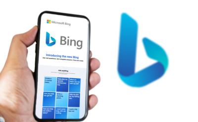 This image depicts the Microsoft Bing chatbot in a smartphone with the Bing logo in the background