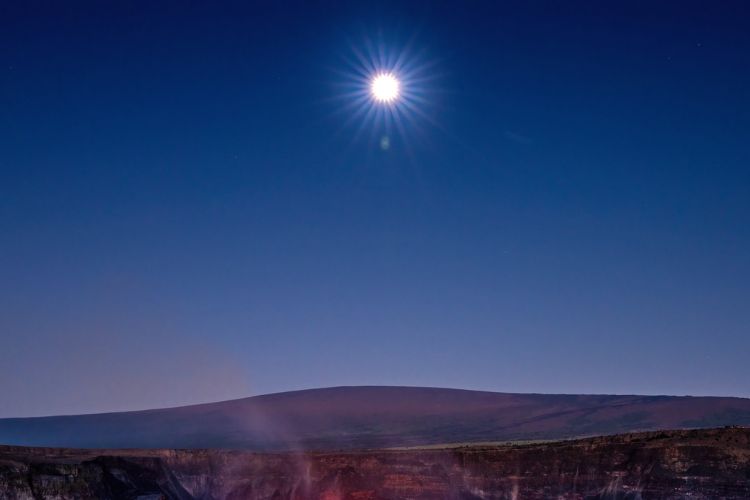 This image depicts a full moon rises over an active caldera in Hawaii Volcanoes National Park