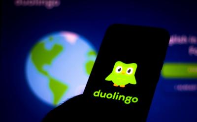 This image portrays the Duolingo app logo on a smartphone with the homepage of the app open on a screen in the background