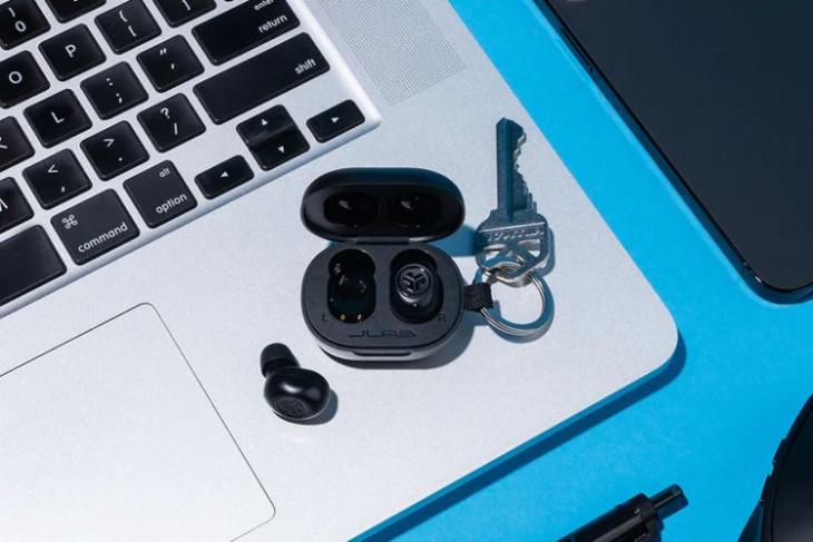 JBuds Mini TWS from JLabs is showcased in this image in black color with a key attached to its keychain loop and placed on top of a laptop