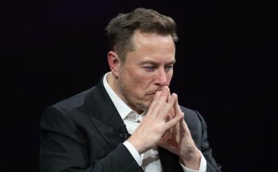 Elon Musk with his hands in front of his face
