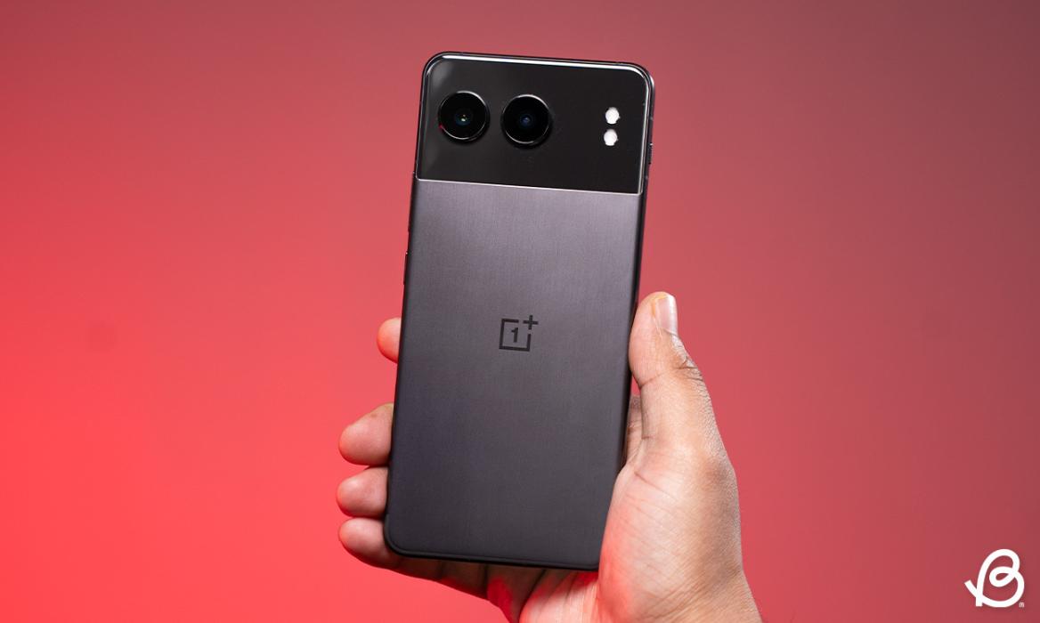 hand holding the OnePlus Nord 4 showing the rear panel in front of a reddish gradient background