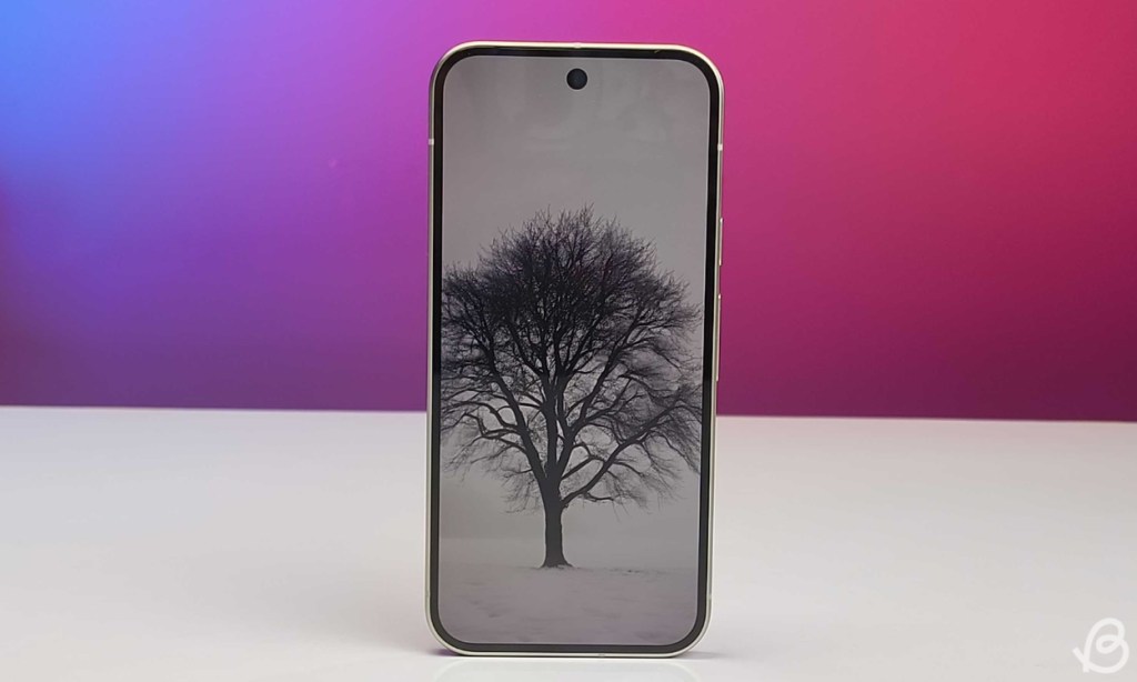 Pixel 9 phone placed upright on a white flat surface with a pink blue gradient background