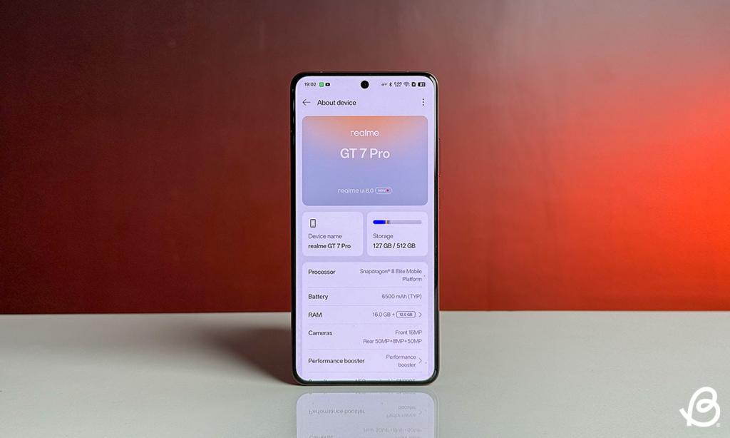 The About device screen on the Realme GT 7 Pro placed on a white desk with orange background