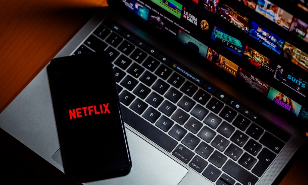 Phone with Netflix logo placed on top an open laptop showing Netflix catalog