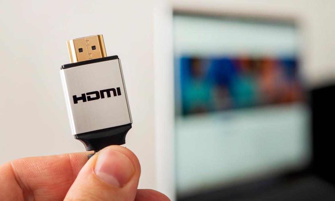 fingers holding HDMI cable in front of a blurred background featuring a TV