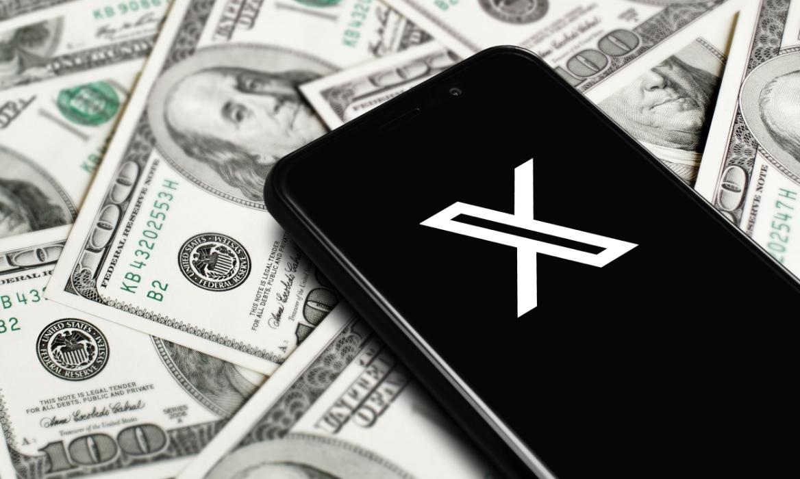 X app logo on a phone that's placed on a pile of US dollars