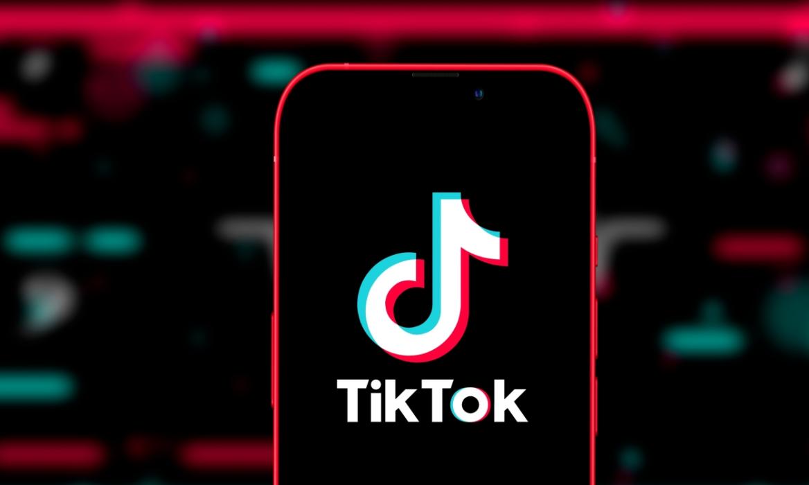 phone with TikTok logo in front of a blurred black background with pink and green elements